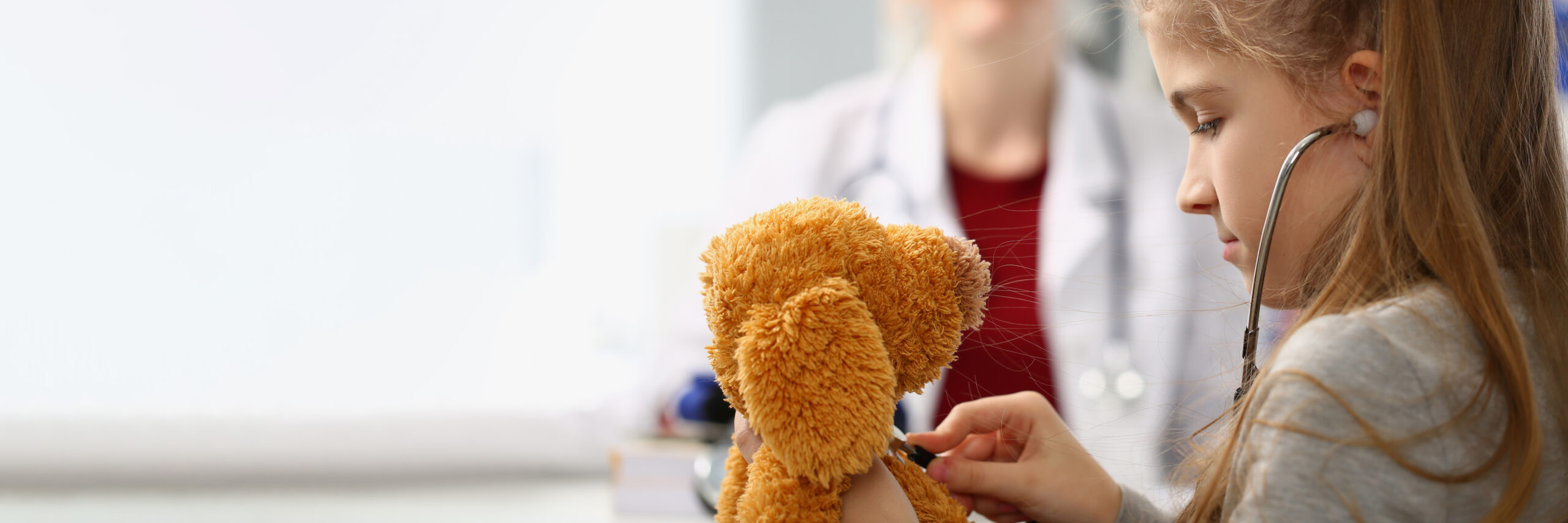 Child listening to a teddy bear’s heartbeat during a pediatric visit
